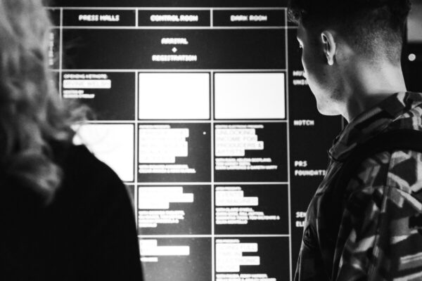 Black and White image of two people looking at the time table of AVA London Electronic Music Conference 2022.