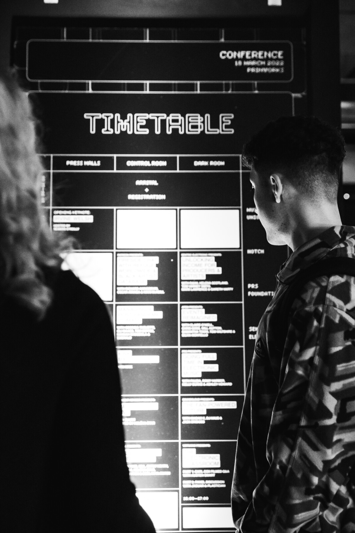 Black and White image of two people looking at the time table of AVA London Electronic Music Conference 2022.