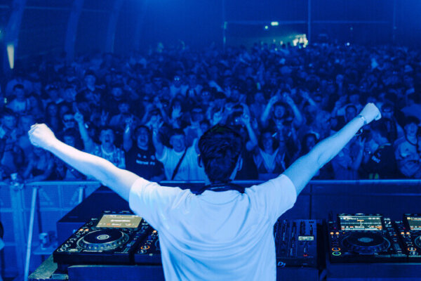 Chris Flannigan performs on the Pumphouse stage at AVA Belfast 2025, raising his arms to a full crowd illuminated in blue light.